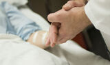 Foto fra hospital, læge tager sengeliggende patients hånd